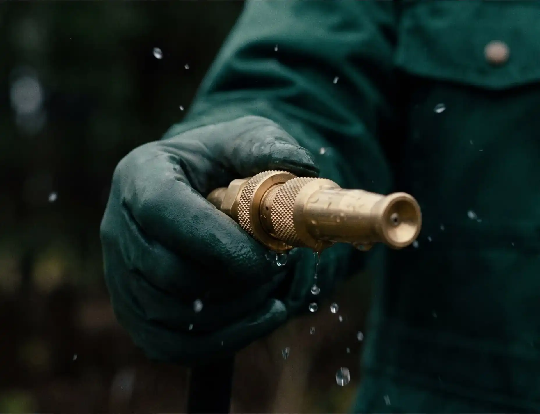 Close-up of a technician's gloved hand adjusting a brass soft-wash nozzle, water droplets in the air