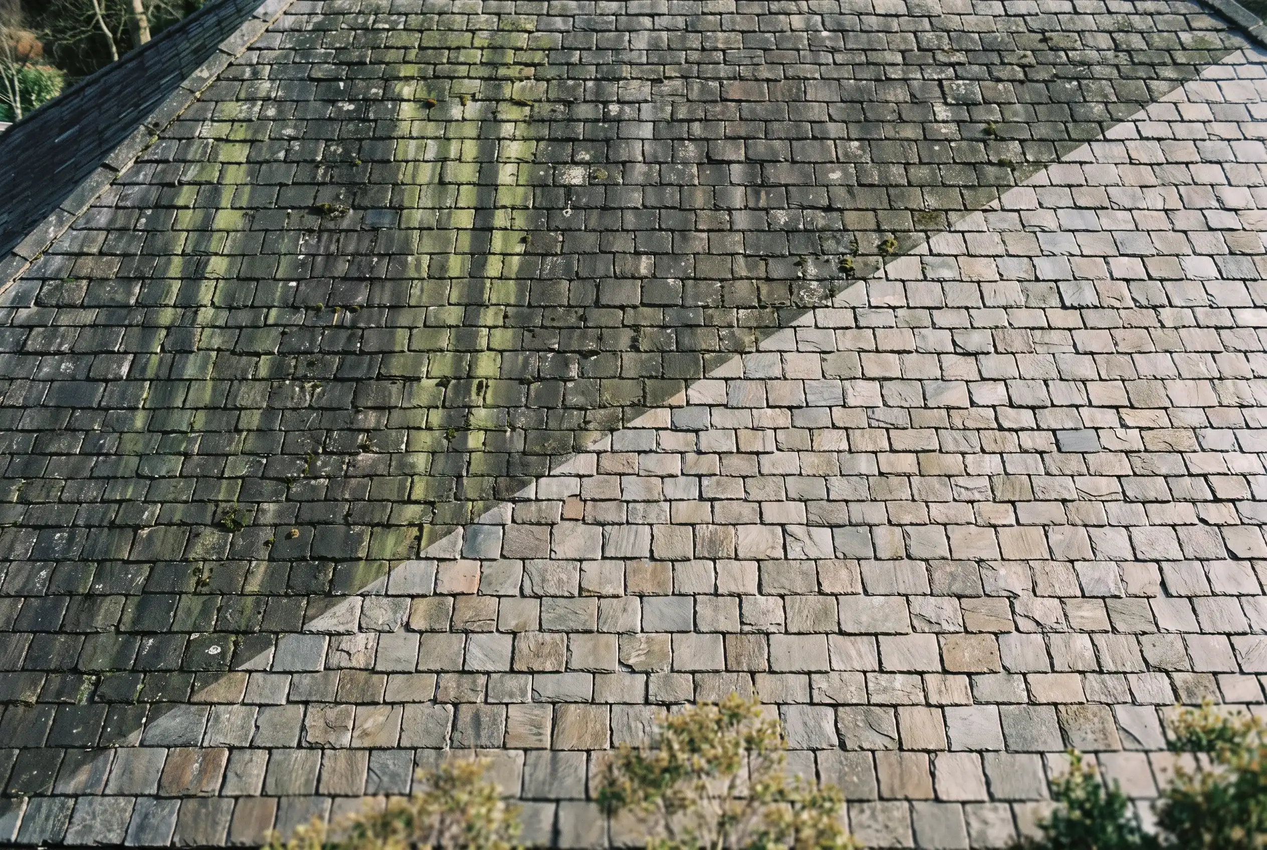 Half-cleaned slate roof showing the dramatic line between algae-streaked and restored shingles